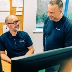 Two Jotron employees discussing in front of the PCs. Two Jotron employees discussing in front of the PCs.