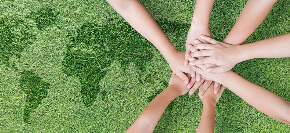 A pile of hands laying on a lawn with an embedded shape of a world map.