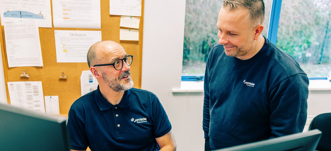 Two Jotron employees discussing in front of the PCs.