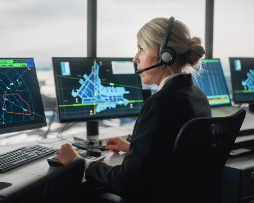 An air traffic controller seated in an ATC tower, monitoring multiple displays.