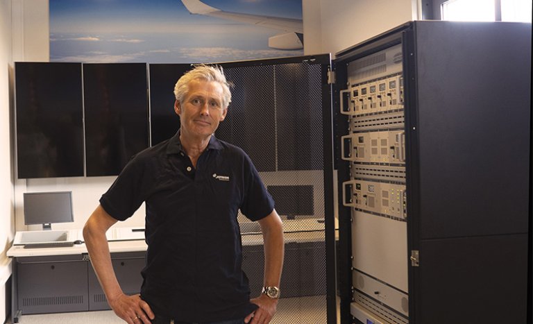 Jotron employee Christian Pindsle standing in front of a  product rack with ATC radios