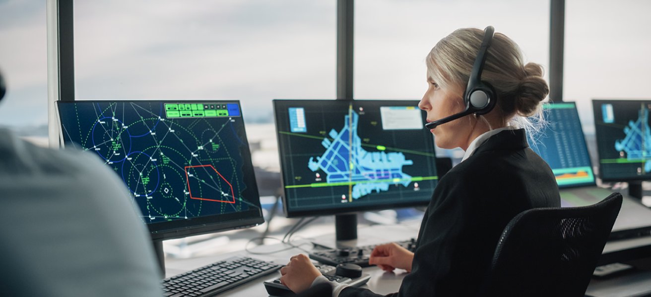 An air traffic controller seated in an ATC tower, monitoring multiple displays.